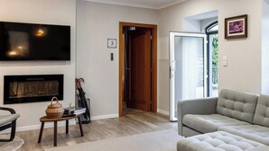 A living room with a flat-screen TV, a fireplace, a sofa, and a door leading to another room.