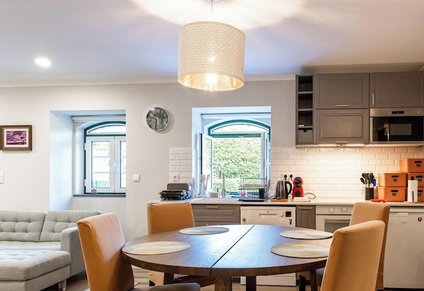 Une cuisine moderne avec un coin repas, comprenant une table ronde entourée de chaises, un luminaire suspendu et une vue par les fenêtres.