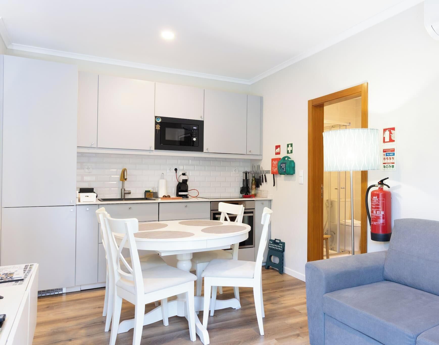 A compact kitchen with white cabinets, a microwave, and a dining area with a white table and chairs.