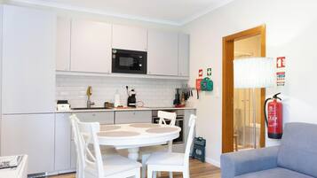 A compact kitchen with white cabinets, a microwave, and a dining area with a white table and chairs.