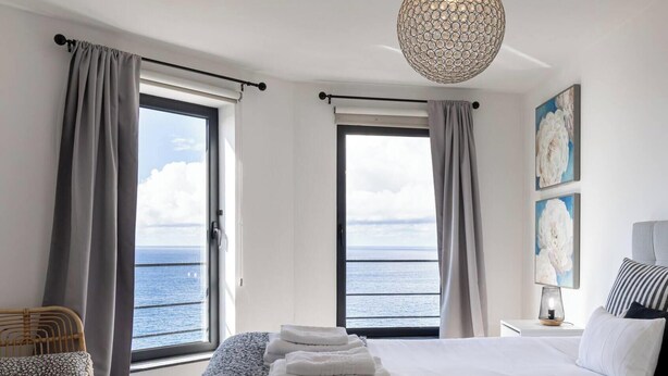 Ein Schlafzimmer mit Bett, Meerblick, einer Chandelüster und Kunstwerken an der Wand.