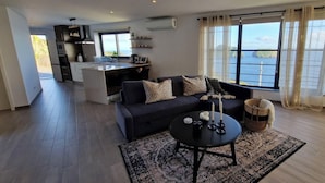 Ein modernes Wohnzimmer mit Sofa, Couchtisch und Blick auf ein Gewässer durch große Fenster.