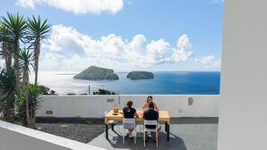 Terras met een tafel en stoelen met uitzicht op de oceaan, met palmbomen en een zicht op twee kleine eilanden.