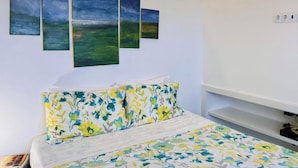 Ein Schlafzimmer mit einem Bett, floralem Bettbezug, einer Wand mit fünf Bildern und einer Decke mit gelben Streifen.