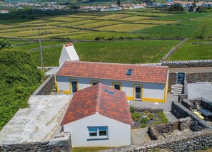 A rural house with a red-tiled roof, stone walls, and a small garden area.