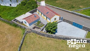 Een huis met twee verdiepingen, voorzien van een rode dakbedekking, een stenen muur en een verharde oprit.