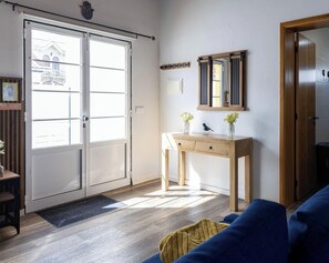 A room with a sliding glass door, a wooden console table with a mirror, a blue sofa, and a wooden floor.