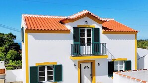 Un edificio de dos pisos con un balcón, una puerta y dos ventanas con persianas.