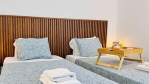 A hotel room with a wooden headboard, two beds with patterned bedding, a bedside table with a lamp, and a tray with breakfast items. - The Biscuit House T2 by PontaNegraAzores (Praia da Vitória)