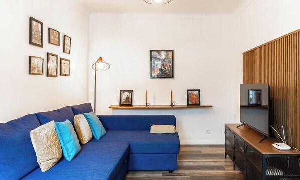 A modern living room with a blue sofa, a TV, and framed artwork on the wall.
