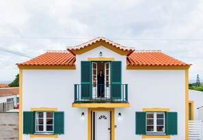A two-story building with a balcony, a white door, and green shutters.