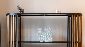 A black metal shelf unit with two decorative figures, a small candle, and books on the bottom shelf. - The Biscuit House T2 by PontaNegraAzores (Praia da Vitória)