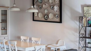 A dining area with a table and chairs, a framed collection of plates on the wall, a bookshelf, and a sofa with cushions. - The North House by Ponta Negra Azores (Biscoitos)