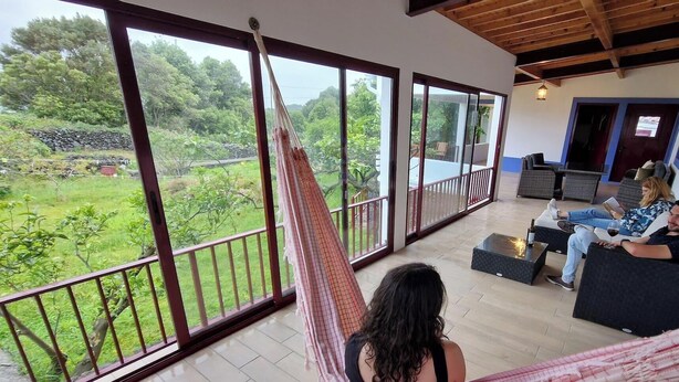 Ein Zimmer mit einer Hängematte, einem Balkon mit Blick auf Grünflächen und einer Sitzecke für zwei Personen.