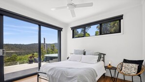 A bedroom with a bed, a nightstand, a chair, and a view of the outdoors.