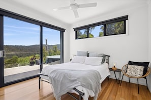 A bedroom with a bed, a nightstand, a chair, and a view of the outdoors.