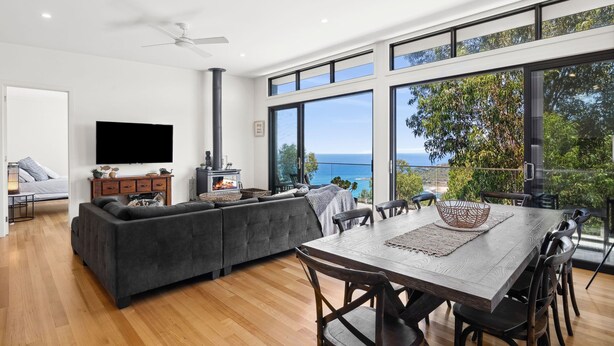 A modern living room with a large TV, a fireplace, and a dining area with a view of the ocean.