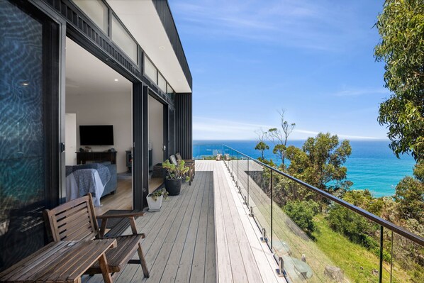 A modern balcony with a view of the ocean, wooden furniture, and potted plants.