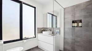 A modern bathroom with a large window, a white sink, a mirror, and a shower area.