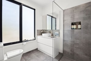 A modern bathroom with a large window, a white sink, a mirror, and a shower area.