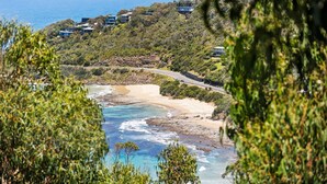 A coastal landscape with a beach, ocean, and a road curving through a hilly area with buildings.