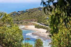 A coastal landscape with a beach, ocean, and a road curving through a hilly area with buildings.