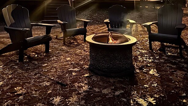 Una cabaña con una sala central amplia y una habitación más pequeña adosada, rodeada de bosque.