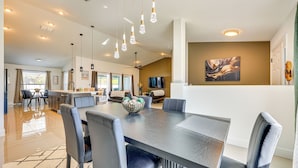 A spacious dining area with a long table and modern chairs, a kitchen in the background, and a ceiling fan. - 8 Mi to Flagler Beach: Home w/ Outdoor Dining! (Palm Coast)