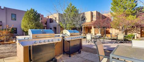 An outdoor patio with two barbecue grills, a table, and chairs.