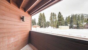 Une cabane en bois avec une fenêtre donnant sur un paysage enneigé et un petit bâtiment visible au loin.
