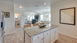 A modern kitchen with white cabinetry, granite countertops, and a dining area with a chandelier. - Endless Summer: Windmark Beach Home Steps to Shore (Port St. Joe)