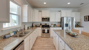 A kitchen with white cabinets, stainless steel appliances, granite countertops, and a large window. - Endless Summer: Windmark Beach Home Steps to Shore (Port St. Joe)