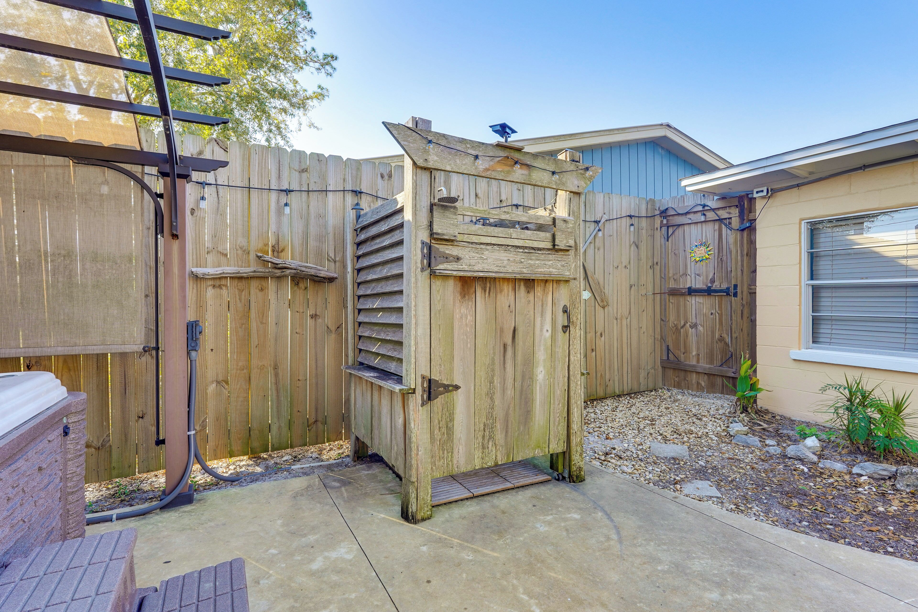 A wooden gate leading to a backyard with a concrete patio, a brick structure, and a wooden fence.