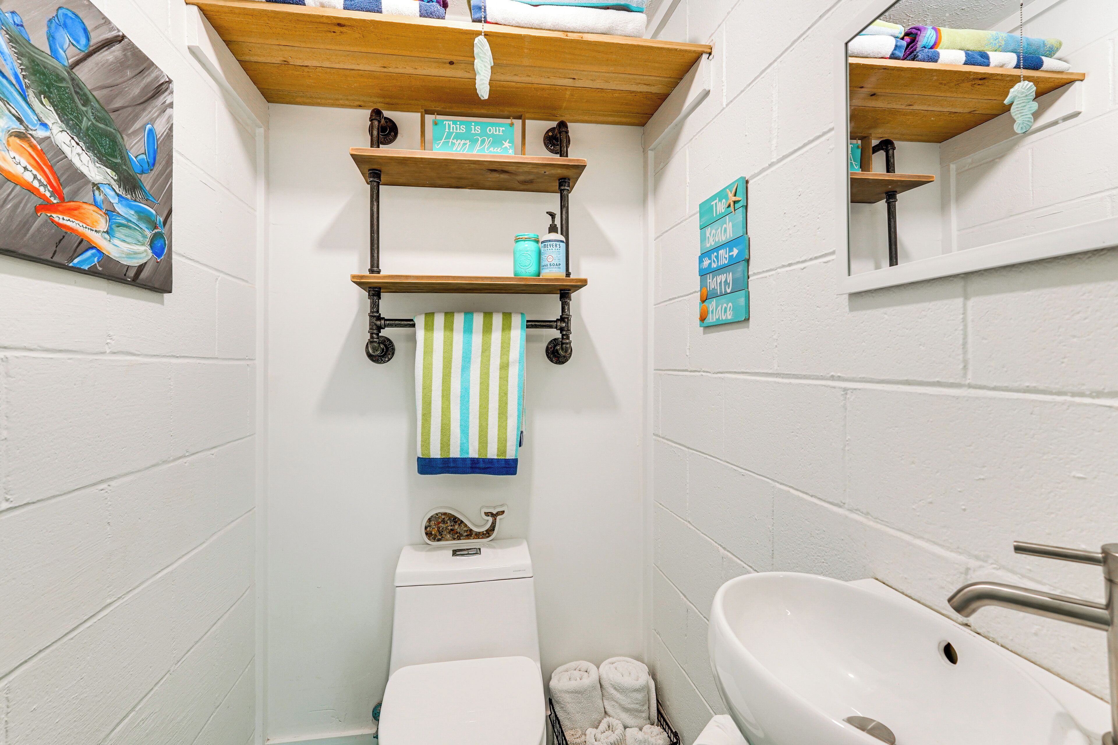 Un baño con inodoro, lavamanos y estantes con toallas y artículos de aseo.