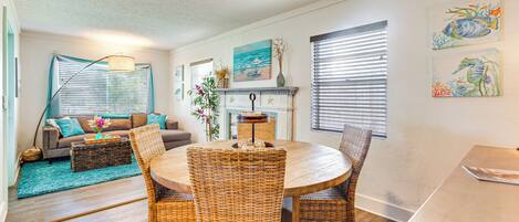 A dining area with a round table and wicker chairs, a ceiling fan, and a fireplace with a mantel.