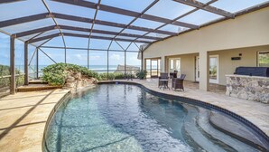 Piscina interna com teto de vidro, deck de ladrilho de pedra e parede de pedra com churrasqueira.