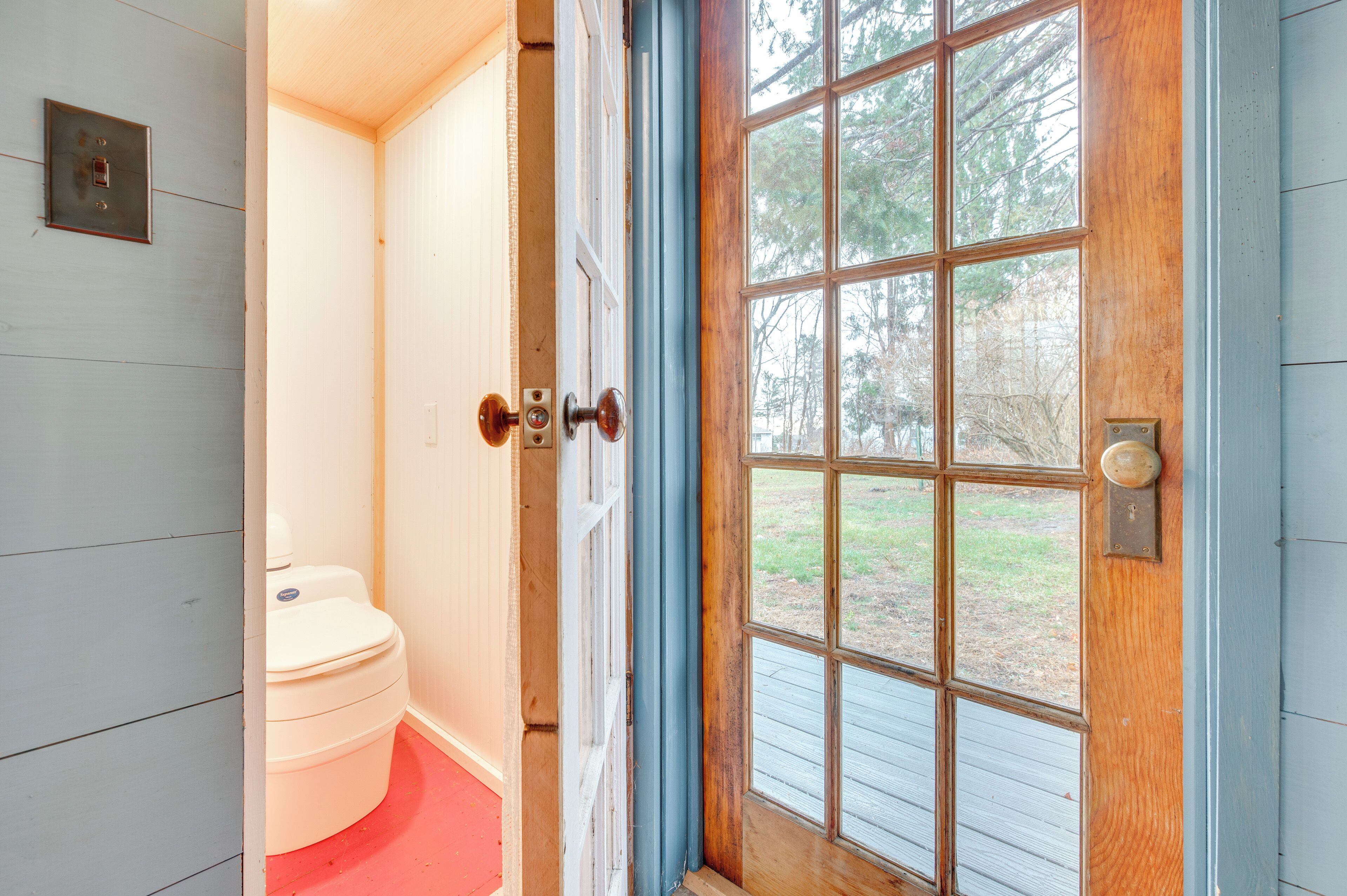 Une porte en bois avec un panneau de verre, des toilettes blanches et un sol rouge.