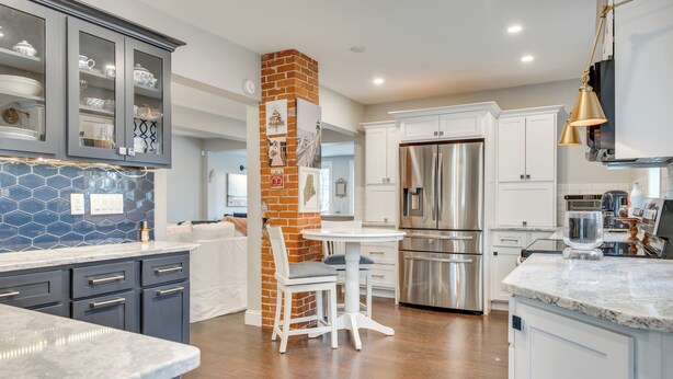 A modern kitchen with grey cabinets, a brick accent wall, a stainless steel refrigerator, and a marble countertop. - 1 Mi to Drakes Island Beach: Cottage w/ Deck! (Wells)