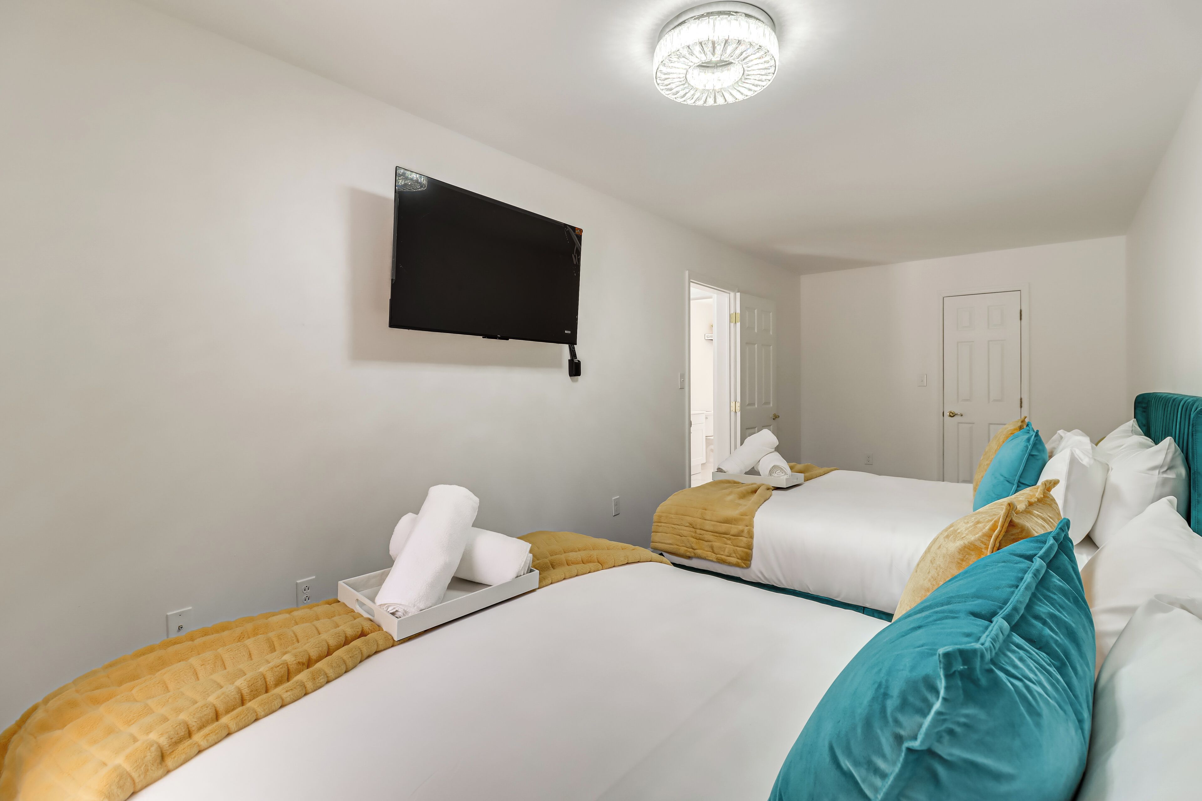 A hotel room with two beds, a flat-screen TV mounted on the wall, and a door to the right.