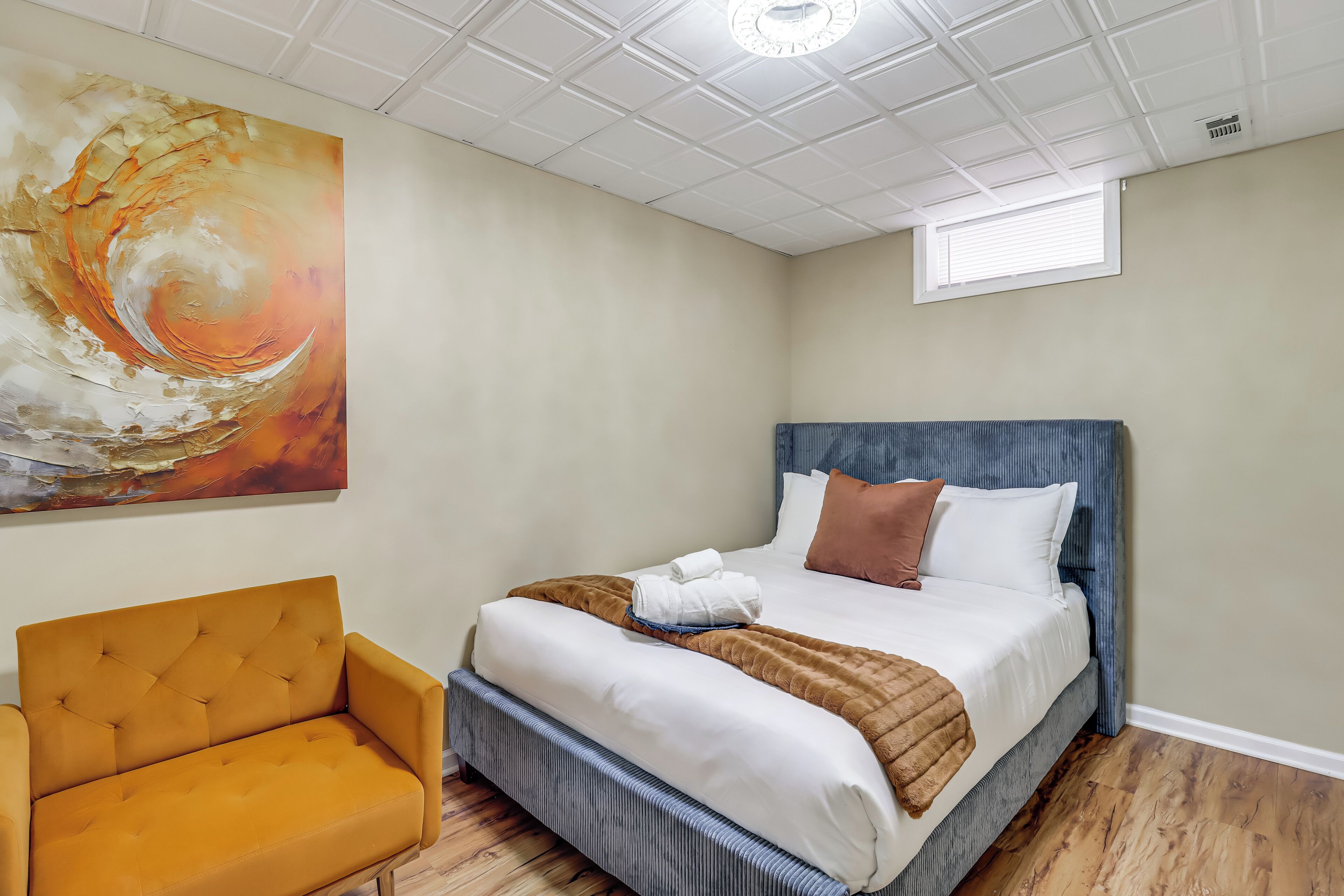 A bedroom with a bed, a sofa, a ceiling light, and a window.