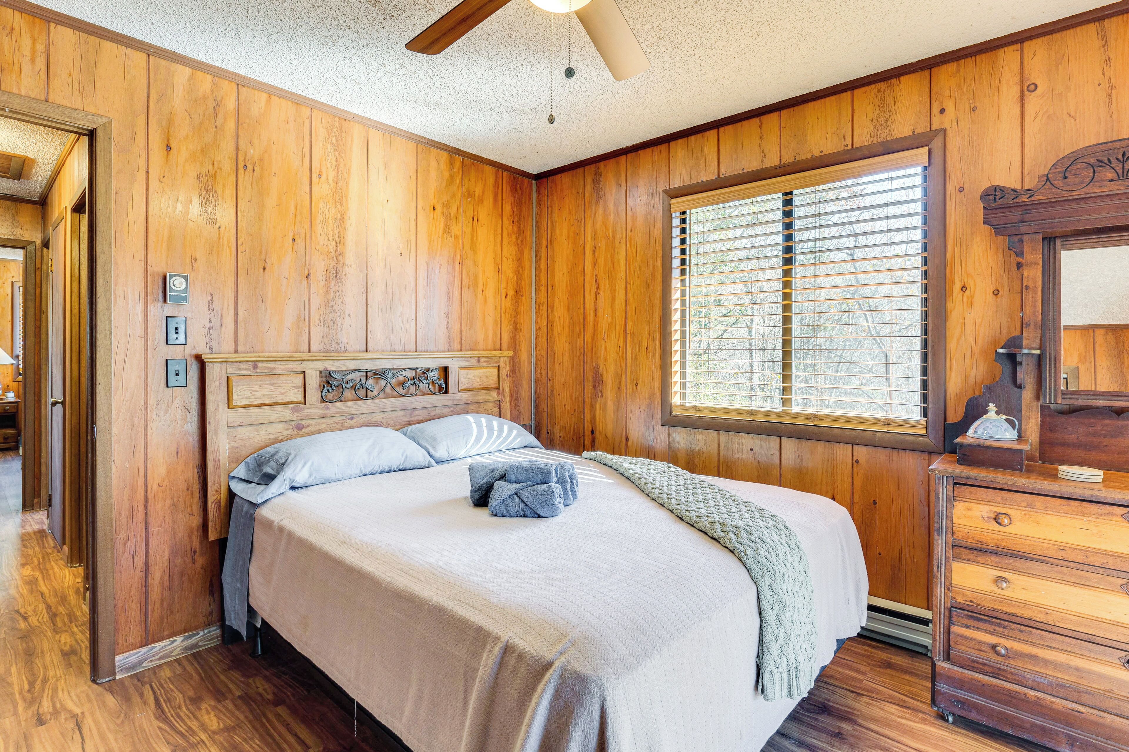 Une chambre aux murs lambrés, avec un lit, une commode et une fenêtre équipée de stores.
