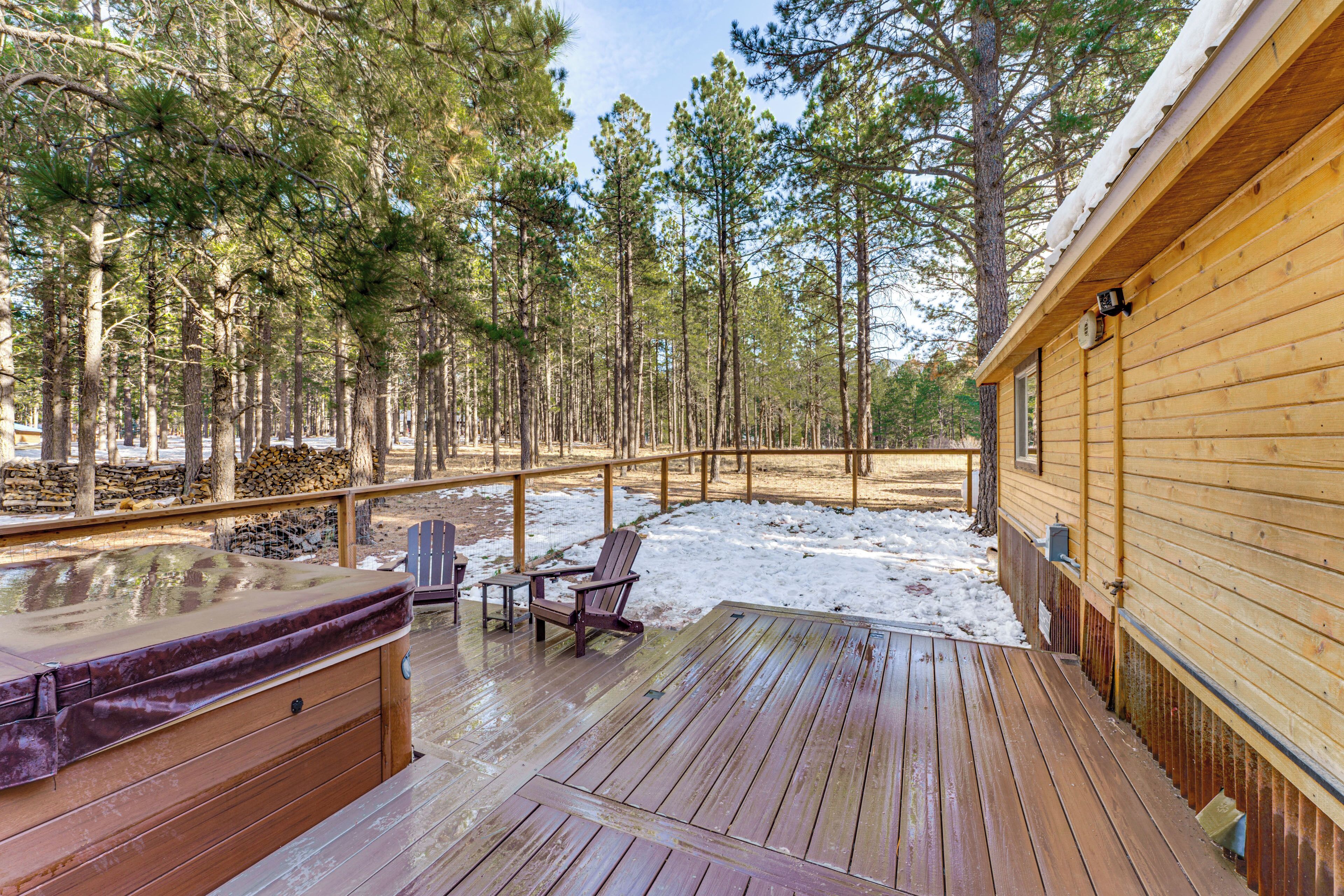 Una terraza de madera con un jacuzzi, sillas y vista a un bosque.