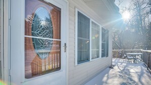 Een huis met een houten deur en grote ramen, een overdekte veranda met een tafel en stoelen, en een sneeuwbedekt terras.