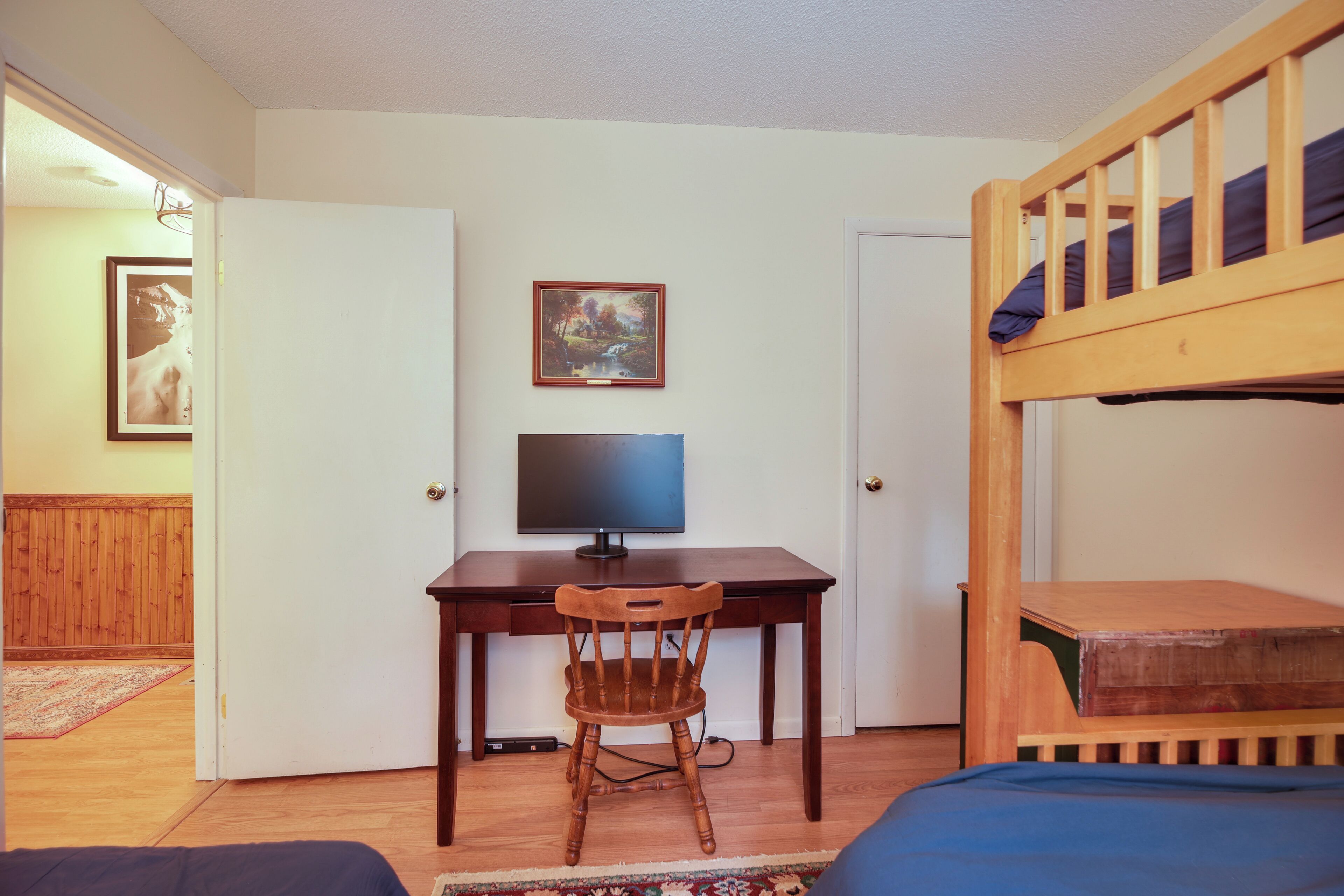 Quarto com cama de solteiro e beliche, uma escrivaninha com cadeira, televisão e um quadro na parede.