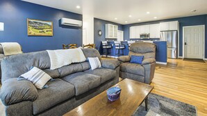 A living room with a grey sofa, a wooden coffee table, and a kitchen area with white cabinets and a stainless steel refrigerator. - 2 Mi to Lake Michigan: Fire Pit, Grill, Patio! (Green Bay)
