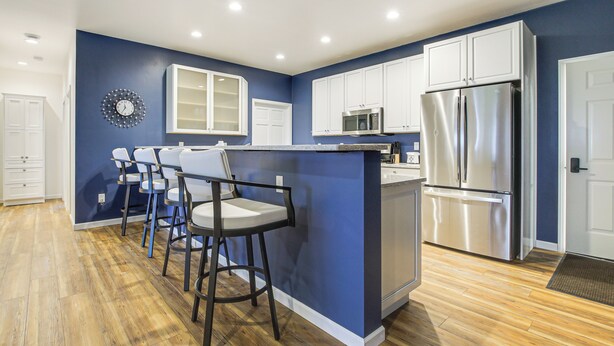 A modern kitchen with a blue accent wall, white cabinetry, a stainless steel refrigerator, and a bar area with stools. - 2 Mi to Lake Michigan: Fire Pit, Grill, Patio! (Green Bay)