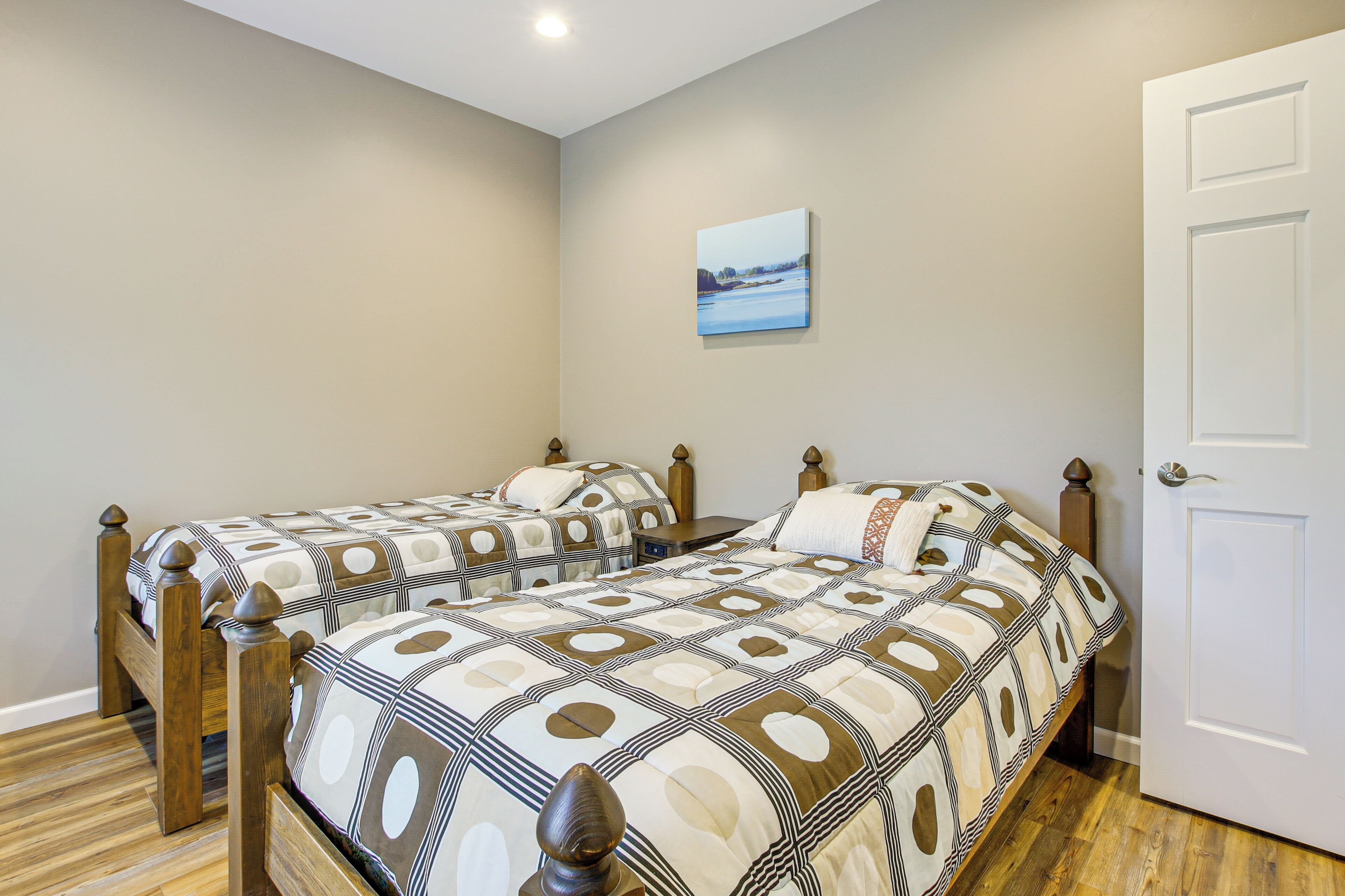A bedroom with two wooden beds, a white door, and a painting on the wall.