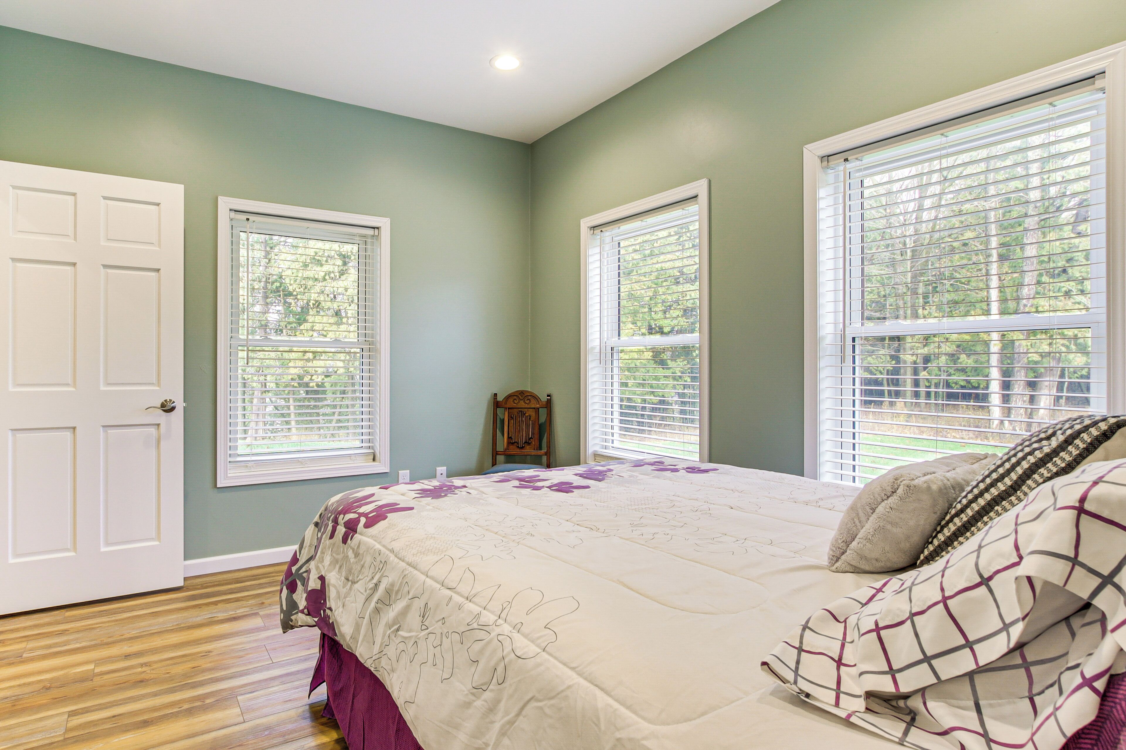A bedroom with a bed, two windows, a door, and a small chair.