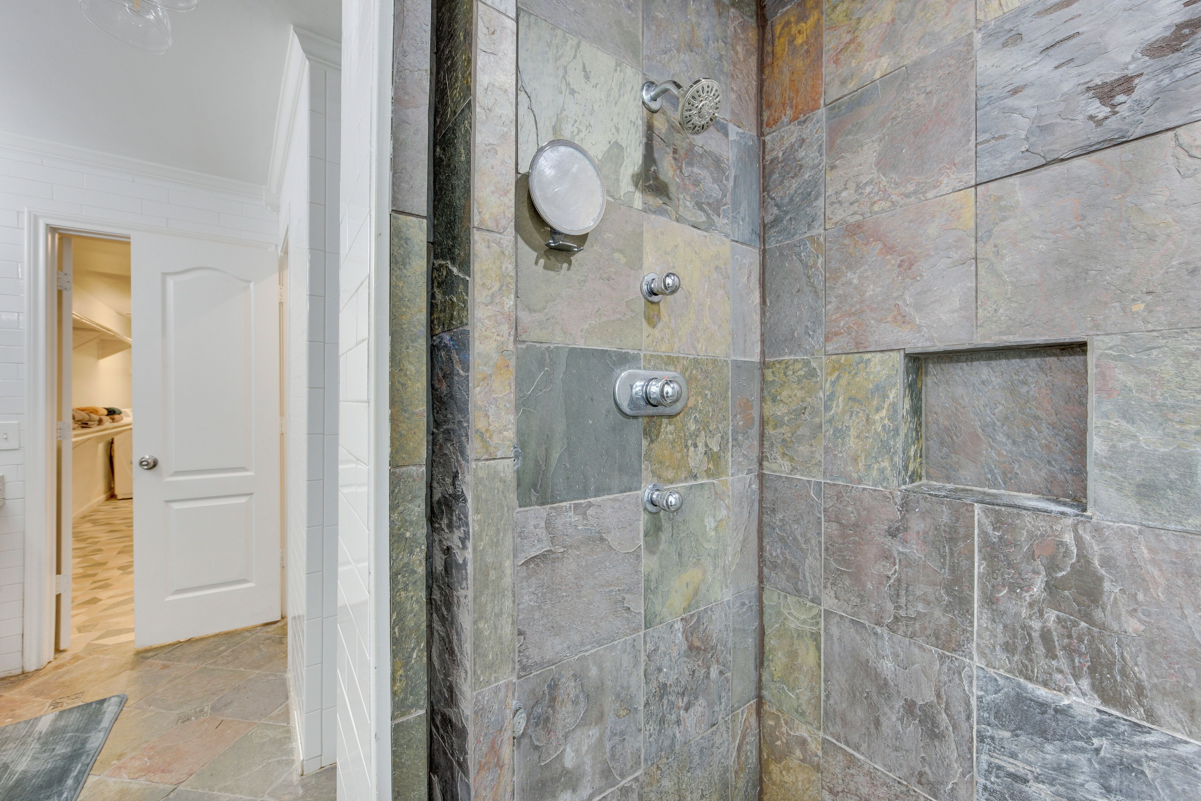 A bathroom with stone tiles, a shower, and a door leading to a hallway.