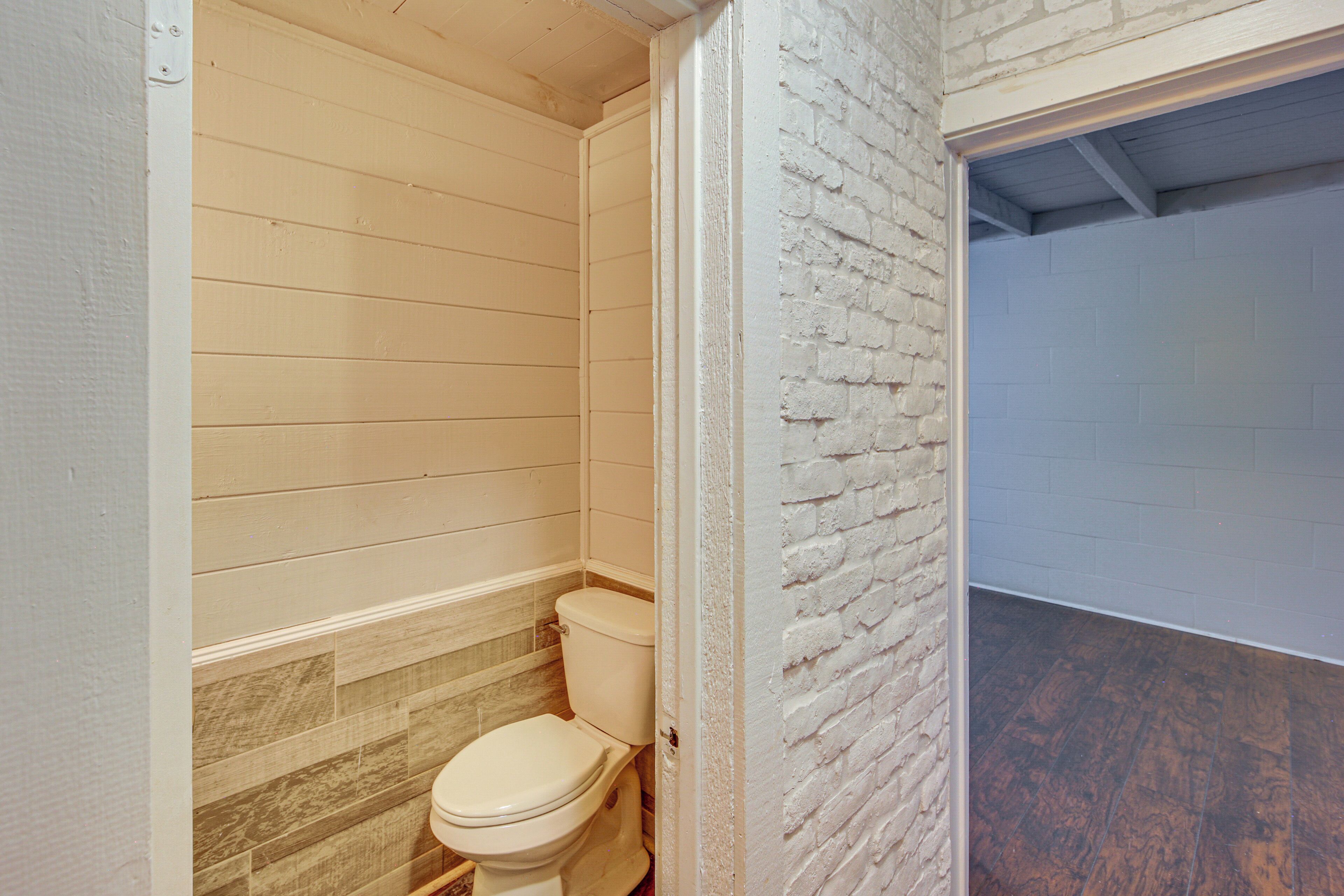 A bathroom with a toilet, wooden walls, and a brick accent wall.